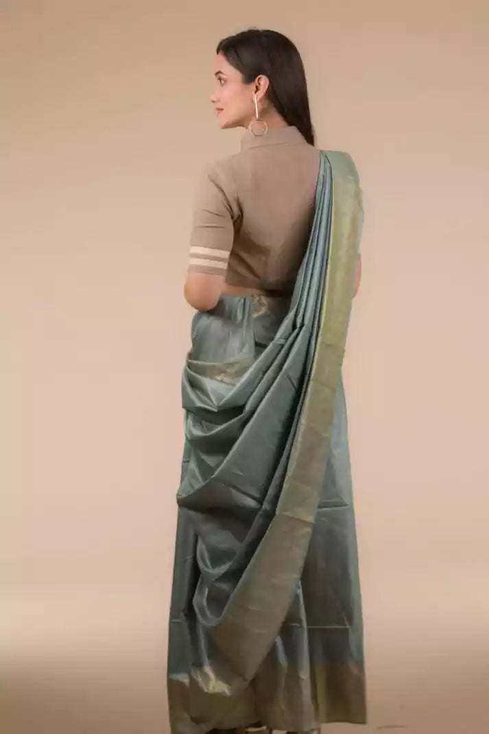 back view of a woman wearing green saree and brown blouse against beige background