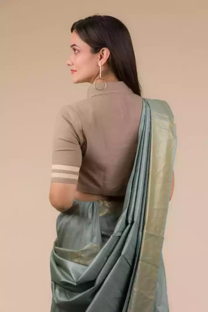 a closure back view of a woman wearing green saree and brown blouse against beige background
