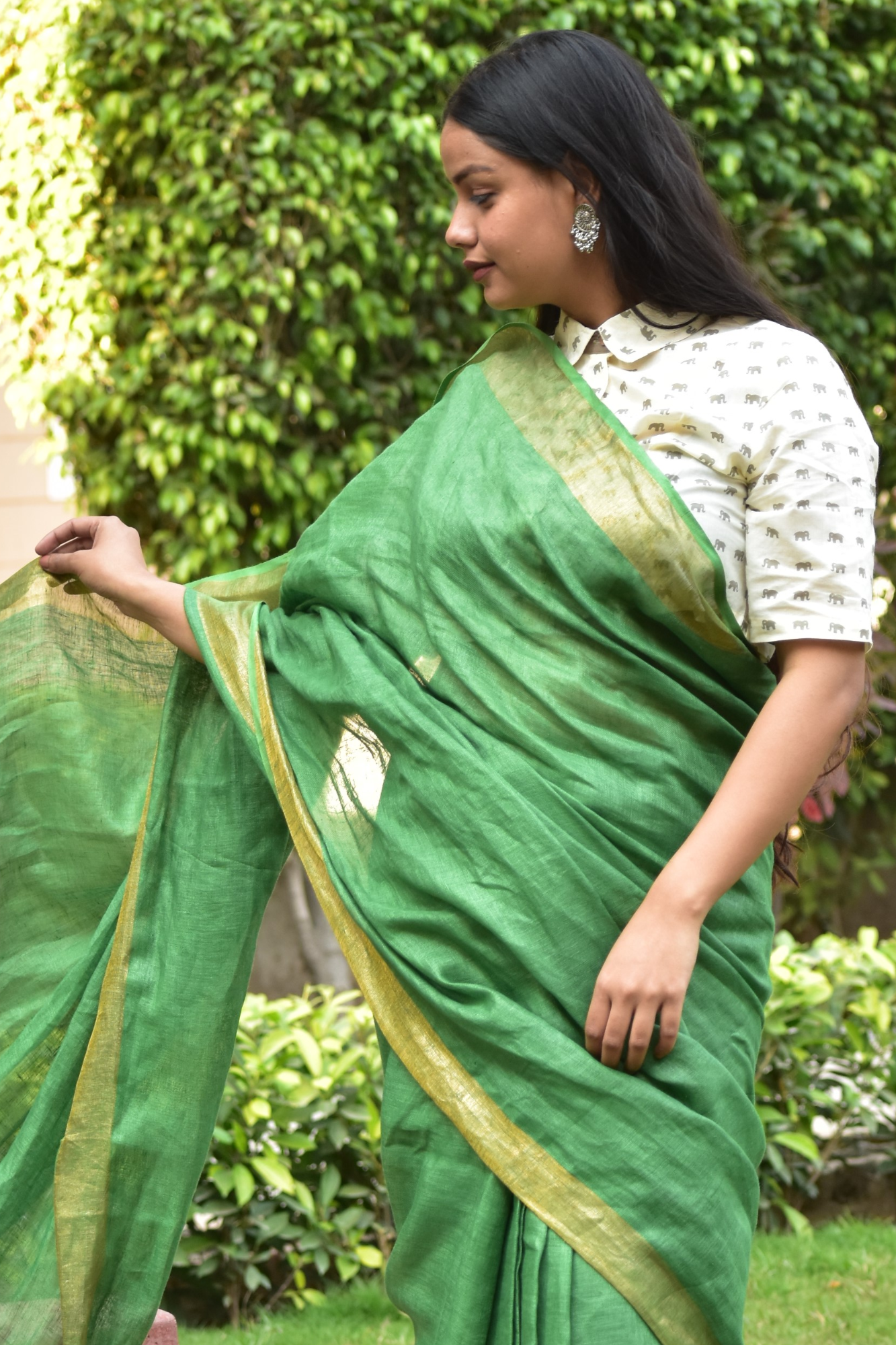 An aesthetic image of lady in Myrtle Linen Saree in Olive Green, womens workwear standing in a garden