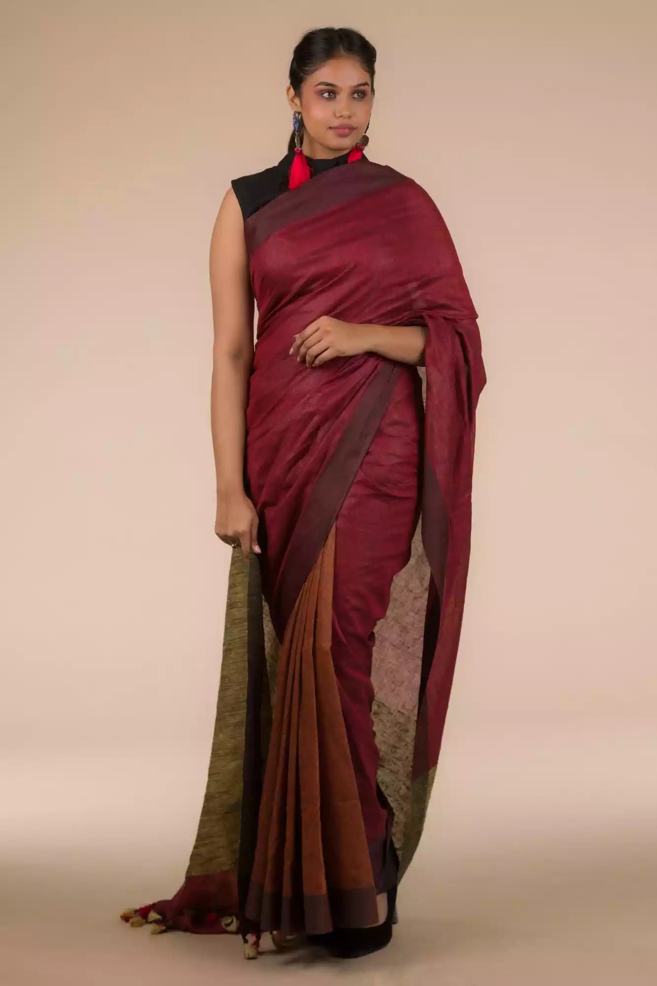 A model in Earthy Brown Pure Linen Saree with Maroon Pleats and Anchal in Beige a womens workwear is standing  against a beige background