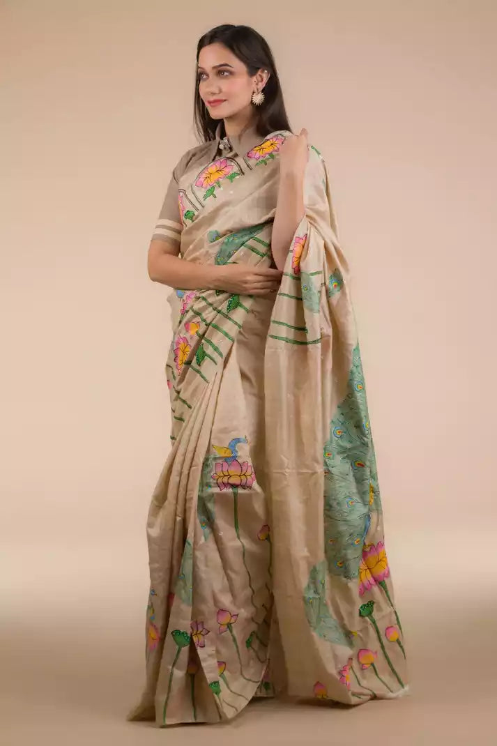 A model in Hand-painted Patachitra Lotus & Peacock design Pure Tussar Saree in Beige a womens workwear is standing  against a beige background