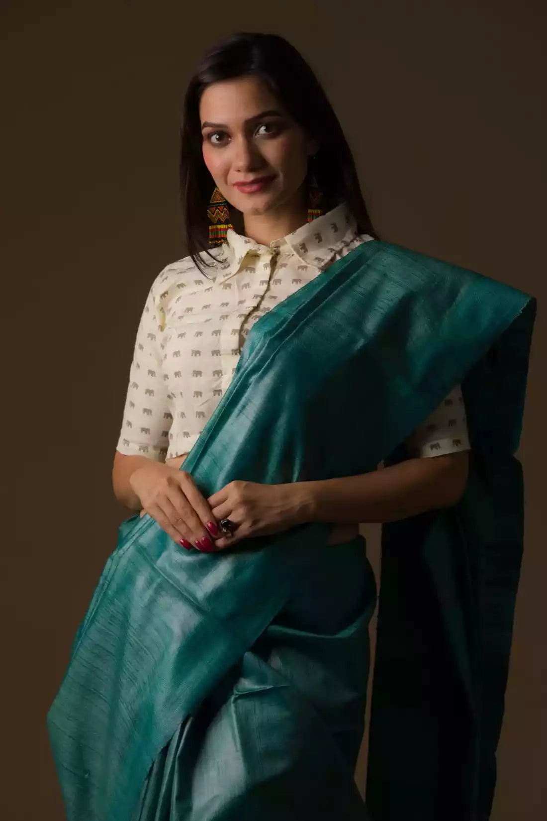 A lady in Sea green Plain In Pure Tussar Saree standing against a brown background.