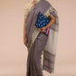 a woman standing in an ethnic grey saree with tie top blouse and a blue color file