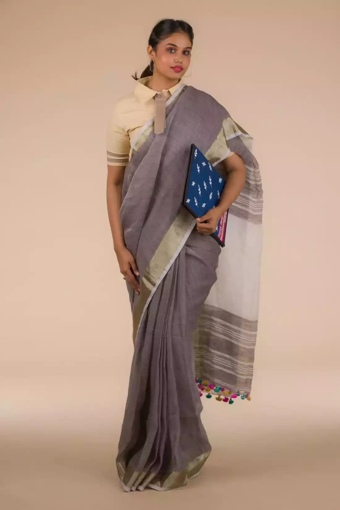 front view of a woman standing in an ethnic grey saree with tie top blouse and a blue color file