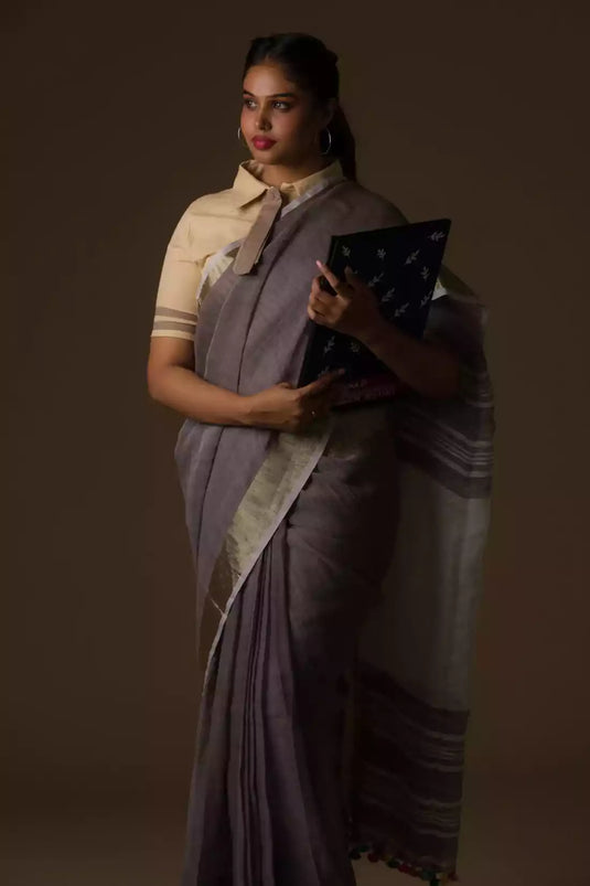 side view of a woman standing in an ethnic grey saree with tie top blouse and a blue color file