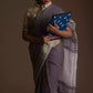 a woman posing in an ethnic grey saree with tie top blouse and a blue color file