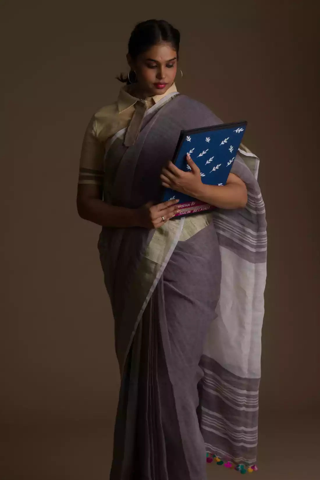 a woman posing in an ethnic grey saree with tie top blouse and a blue color file