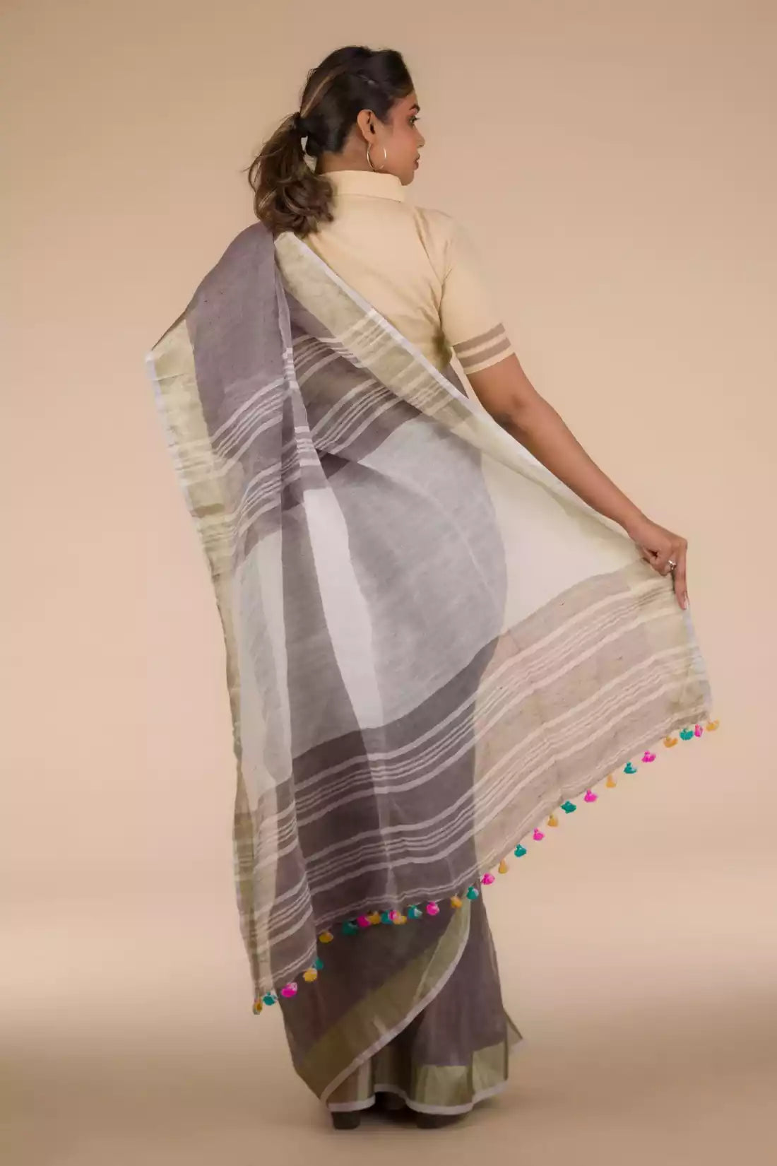 back view of a woman posing in an ethnic grey saree with tie top blouse, flaunting loose end of her saree