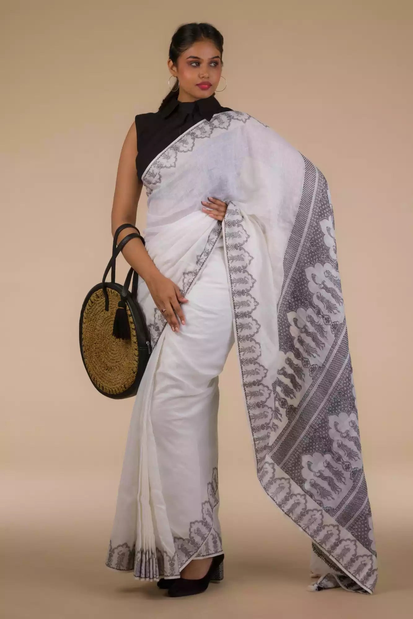 A lady in  Baluchari Resham Thread Linen Saree in White, womens workwear standing against a beige background looking sideways