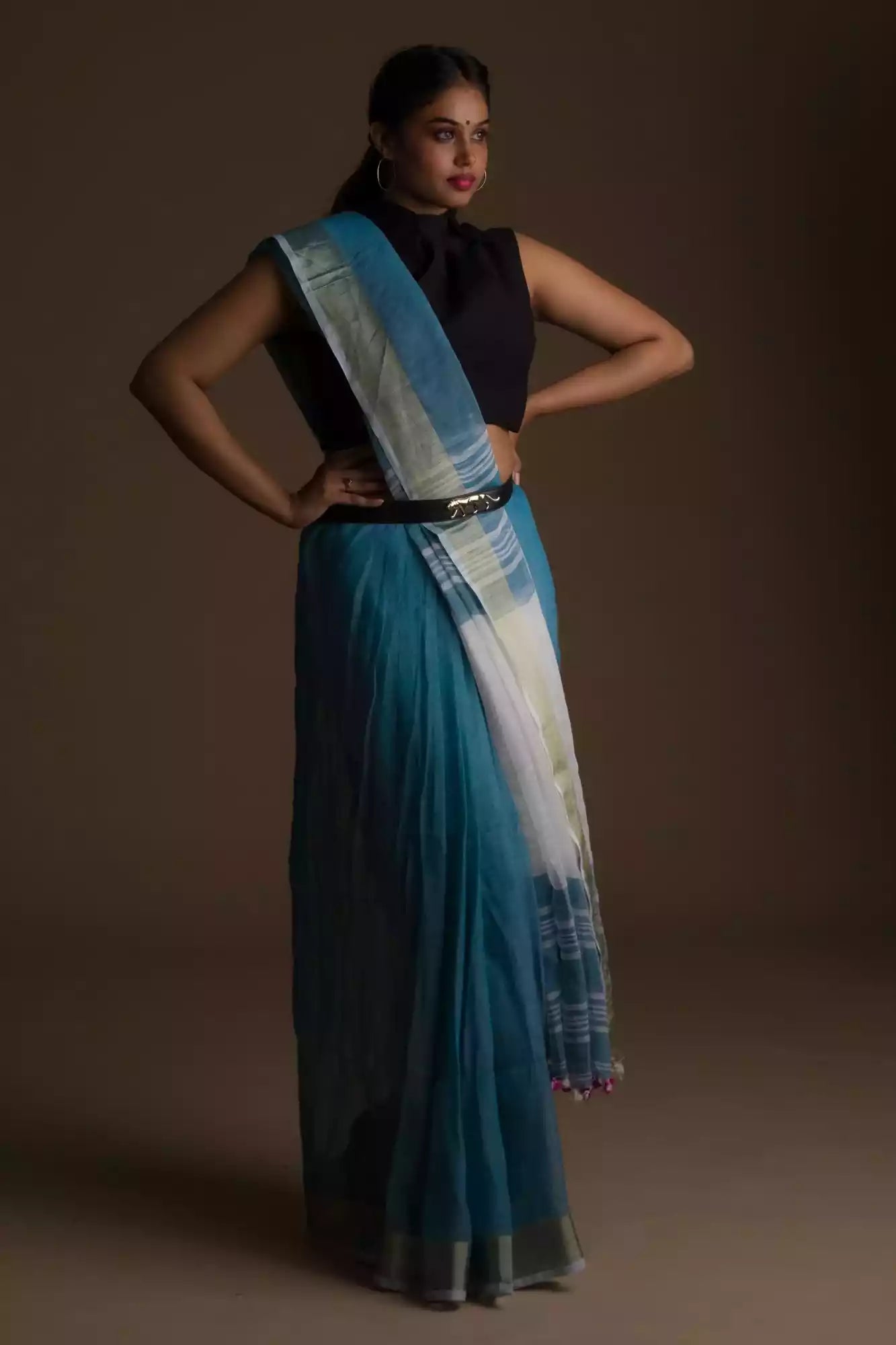 woman wearing a blue saree and a black blouse with stripes at the border and a belt in front of a beige backdrop