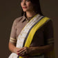 a  closure look of a woman in a white and yellow border saree standing in front of a beige backdrop