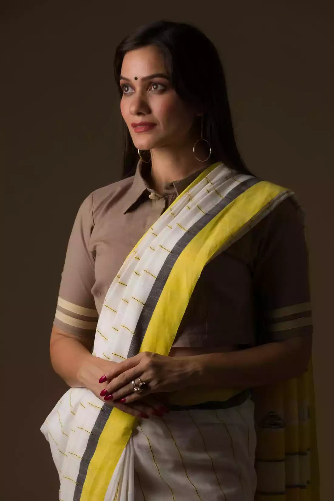 a  closure look of a woman in a white and yellow border saree standing in front of a beige backdrop