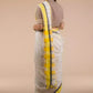 a side view of a  woman in a white and yellow border saree standing in front of a beige backdrop