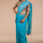 a woman wearing a cyan saree with brown blouse, holding her saree pleats with one hand