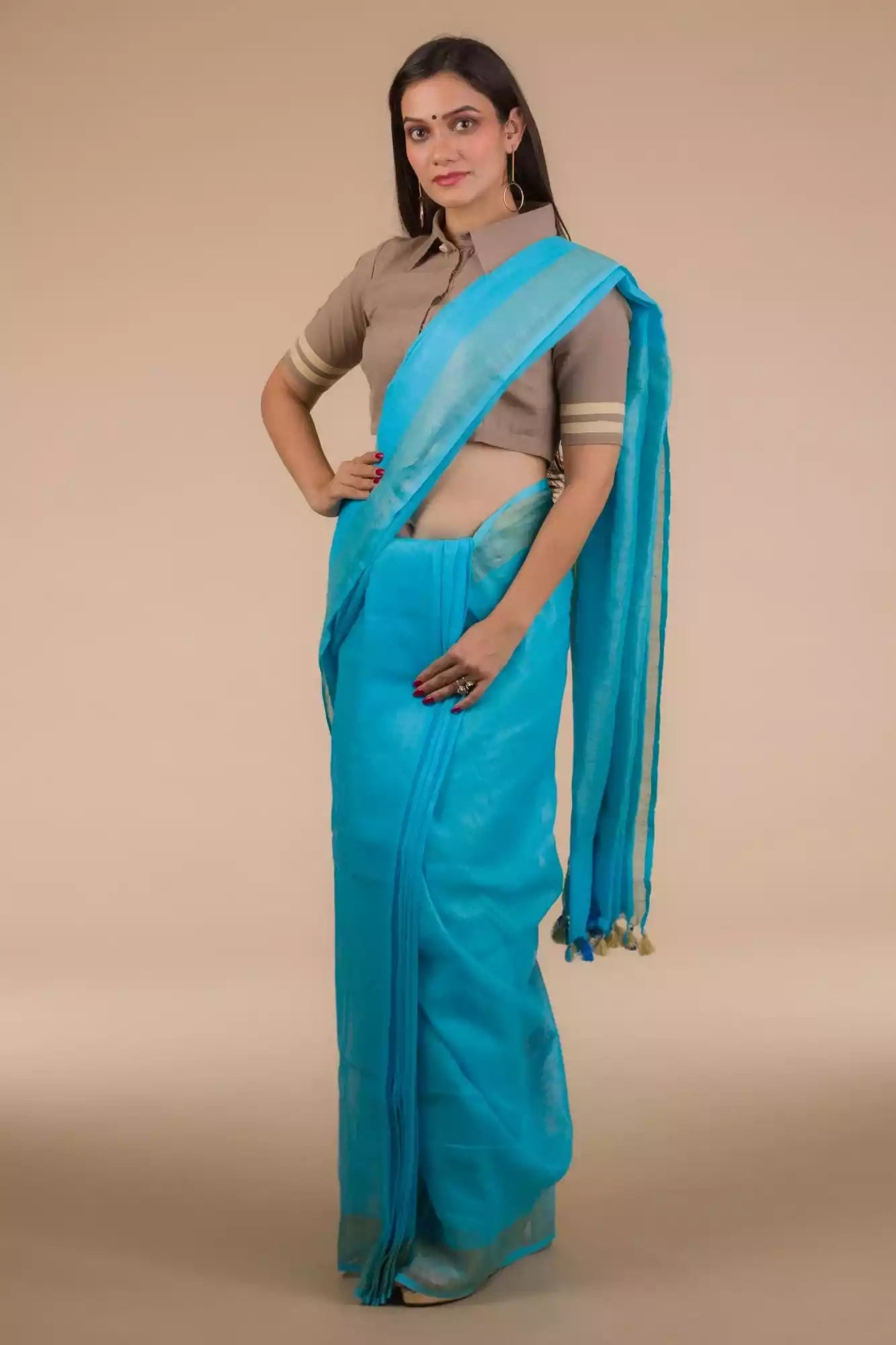 a woman wearing a cyan saree with brown blouse, holding her saree pleats with one hand