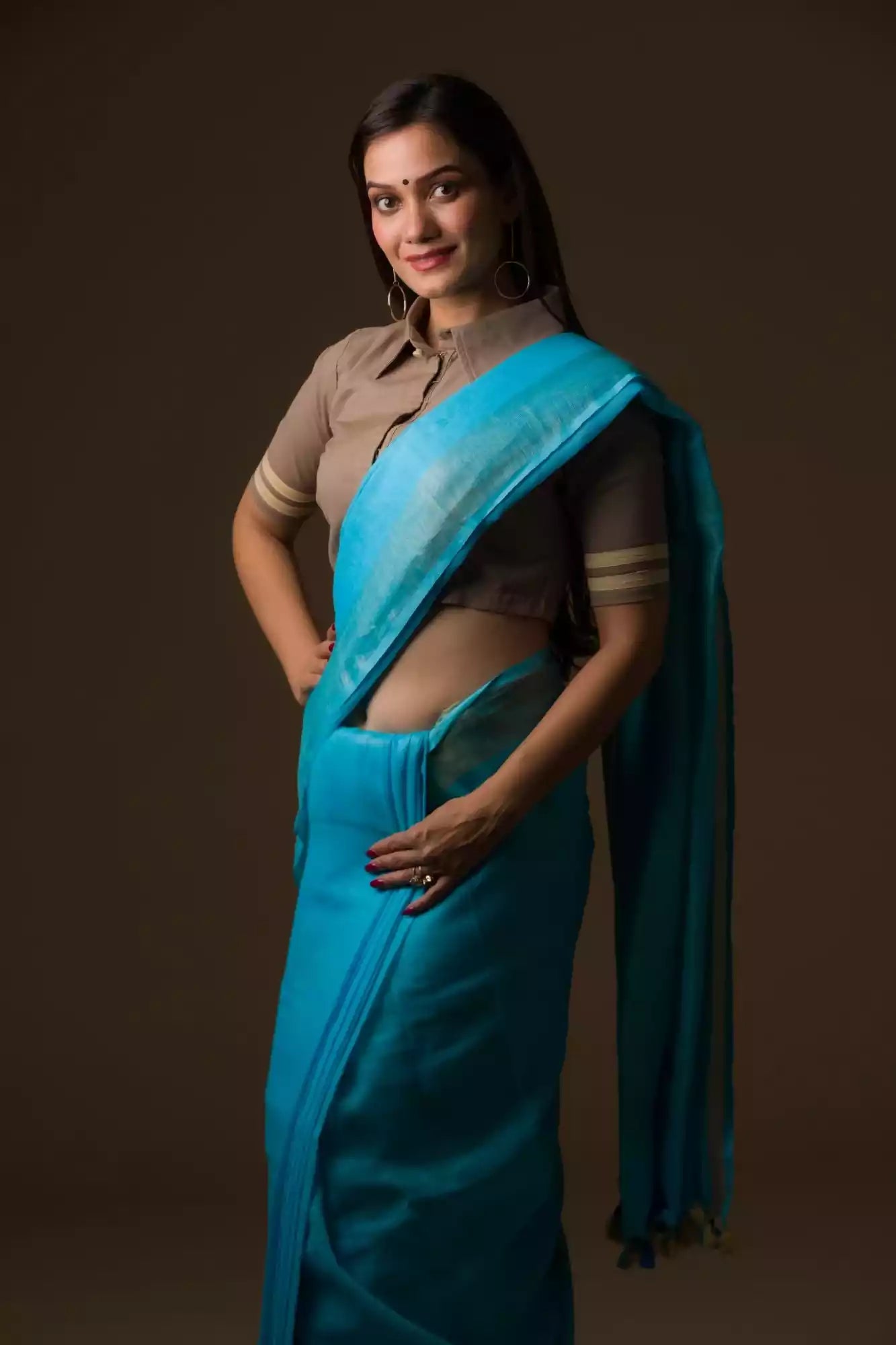 front view of a woman wearing a cyan saree with brown blouse, holding her saree pleats with one hand