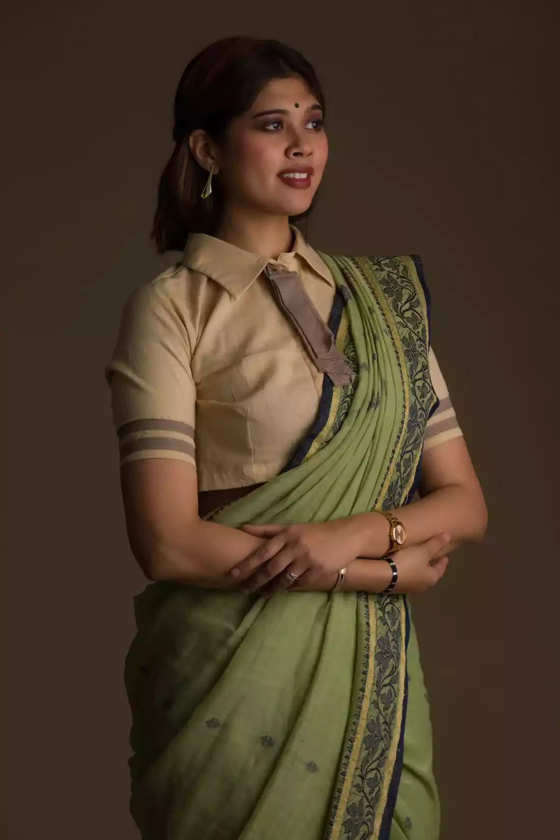 A lady in Myrtle Linen Saree in Olive Green, womens workwear standing against a tan background sidewaysn