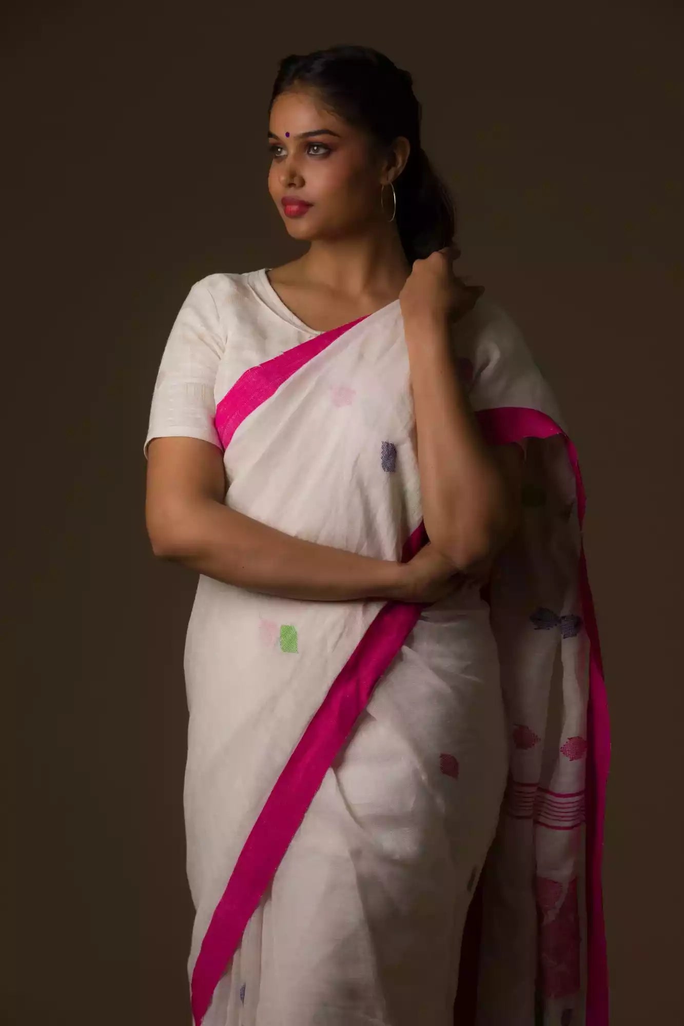 a woman standing in a white saree with pink polka dot work on it and the bottom half