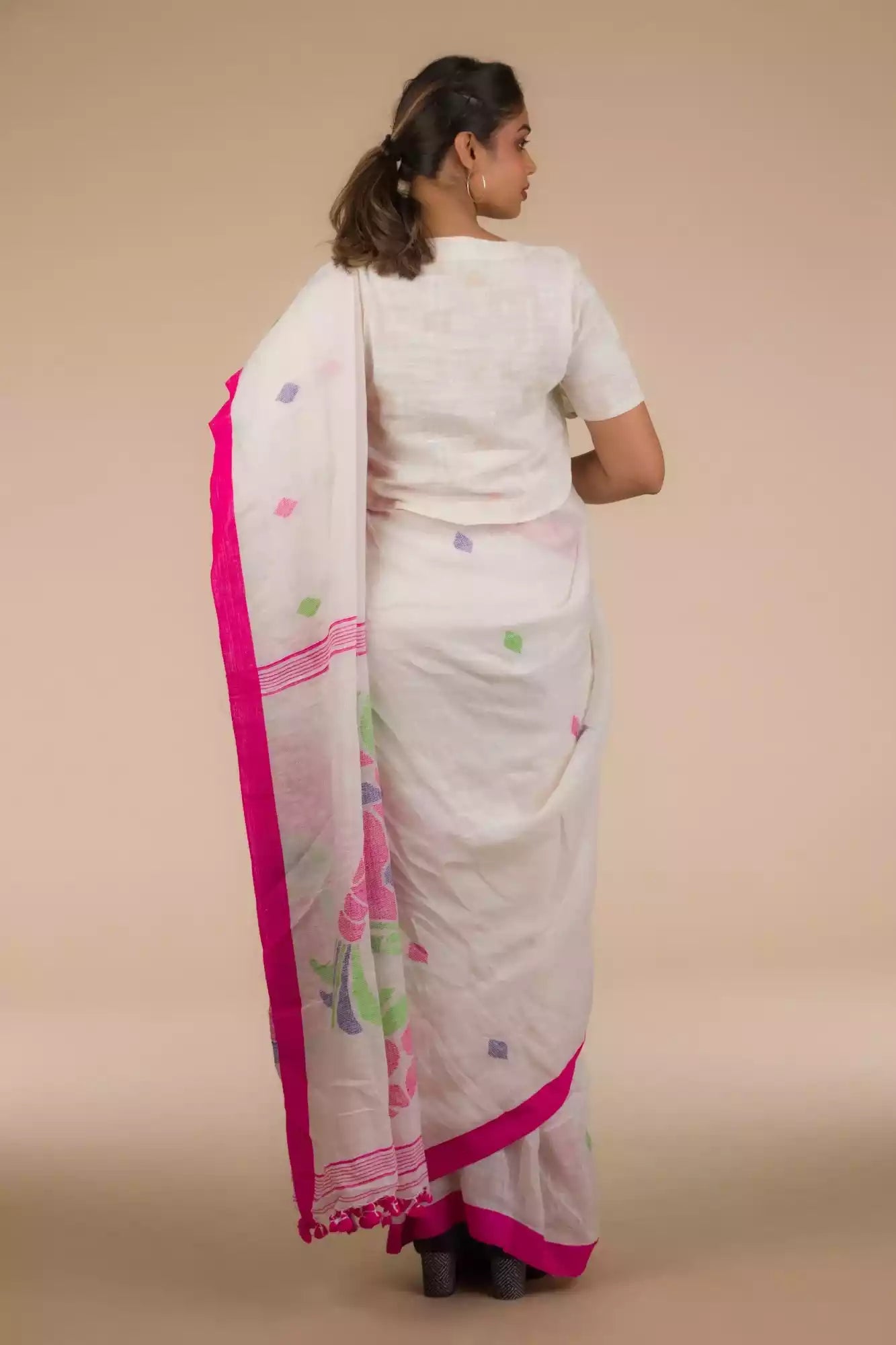 back view of a woman wearing a white saree with pink polka dot work on it and the bottom half