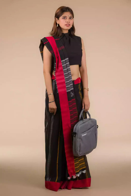 a woman standing in an ethnic black and red saree with striped fabric on the bottom and a grey bag at one side