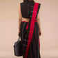 a back view of a woman standing in an ethnic black and red saree with striped fabric on the bottom and a grey bag at one side
