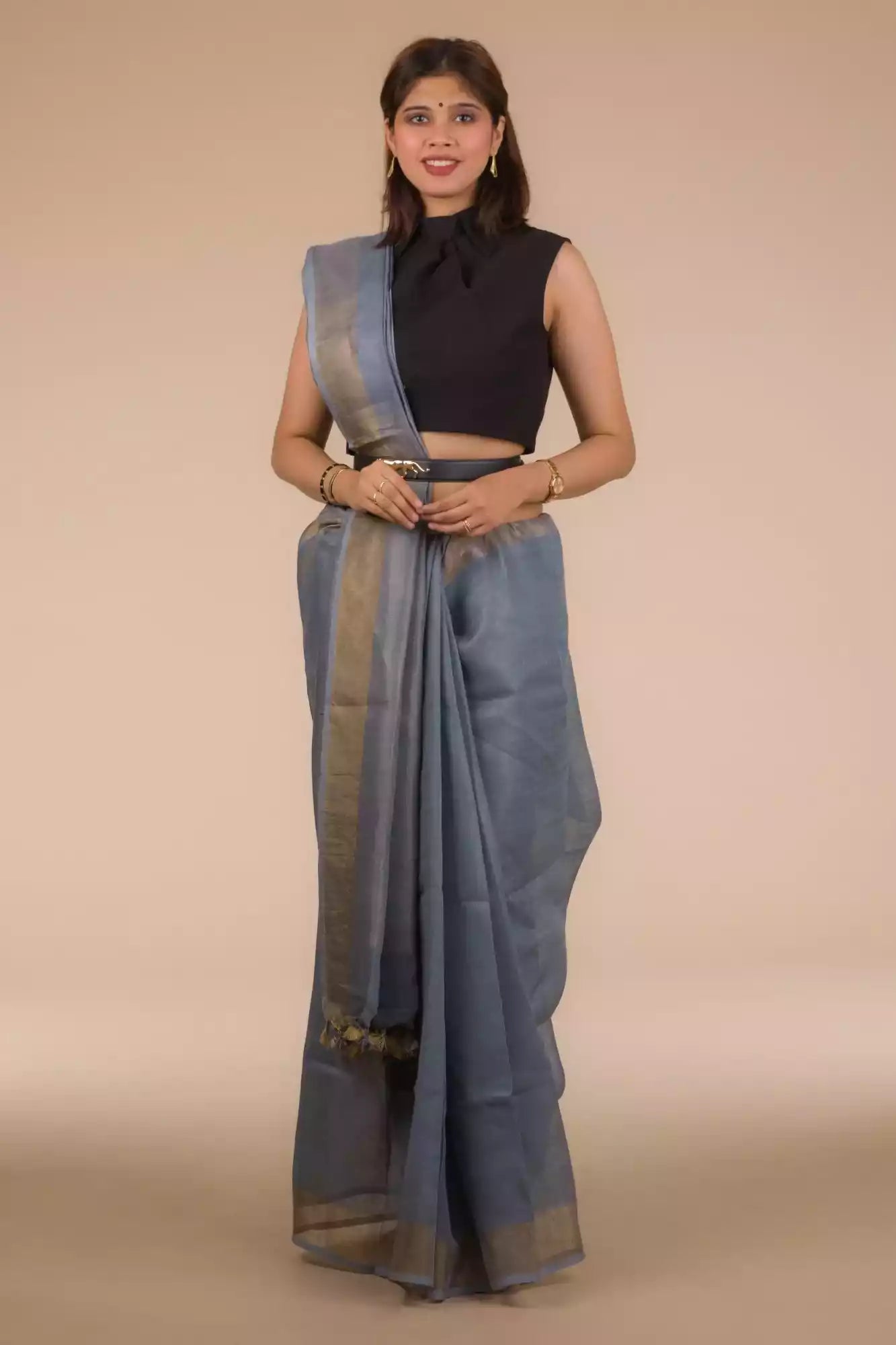 an image of a woman in a grey saree with dark colored sleeveless blouse and a belt around her waist