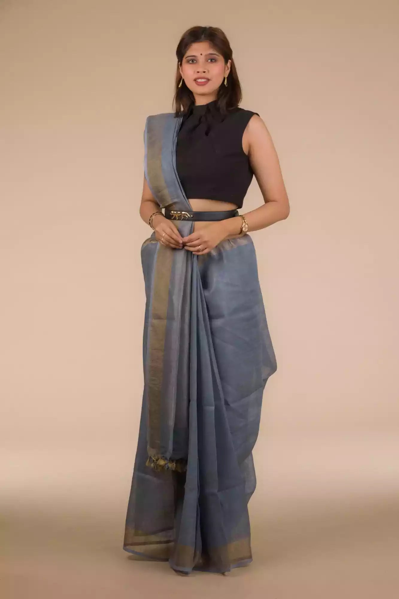 Front view of a woman in a grey saree with dark colored sleeveless blouse and a belt around her waist