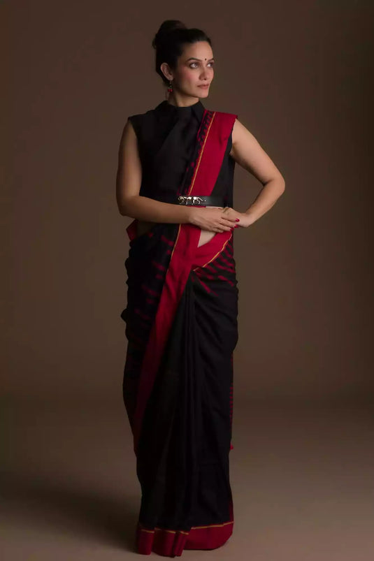 Picture of a woman dressed in black and red stripes color saree with a sleeveless blouse with her hands on her hip
