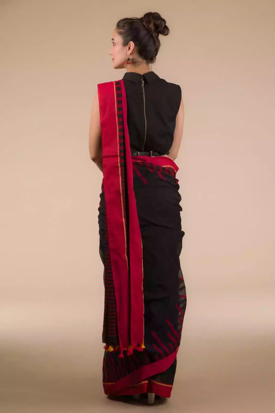a back view of a woman in a black and red saree, posing for a photograph with her hands folded out